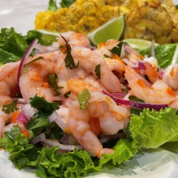 peruvian ceviche made of shrimp, lime and lemon juice, red onion and chopped cilantro and hot peppers on a bed of lettuce with patacones