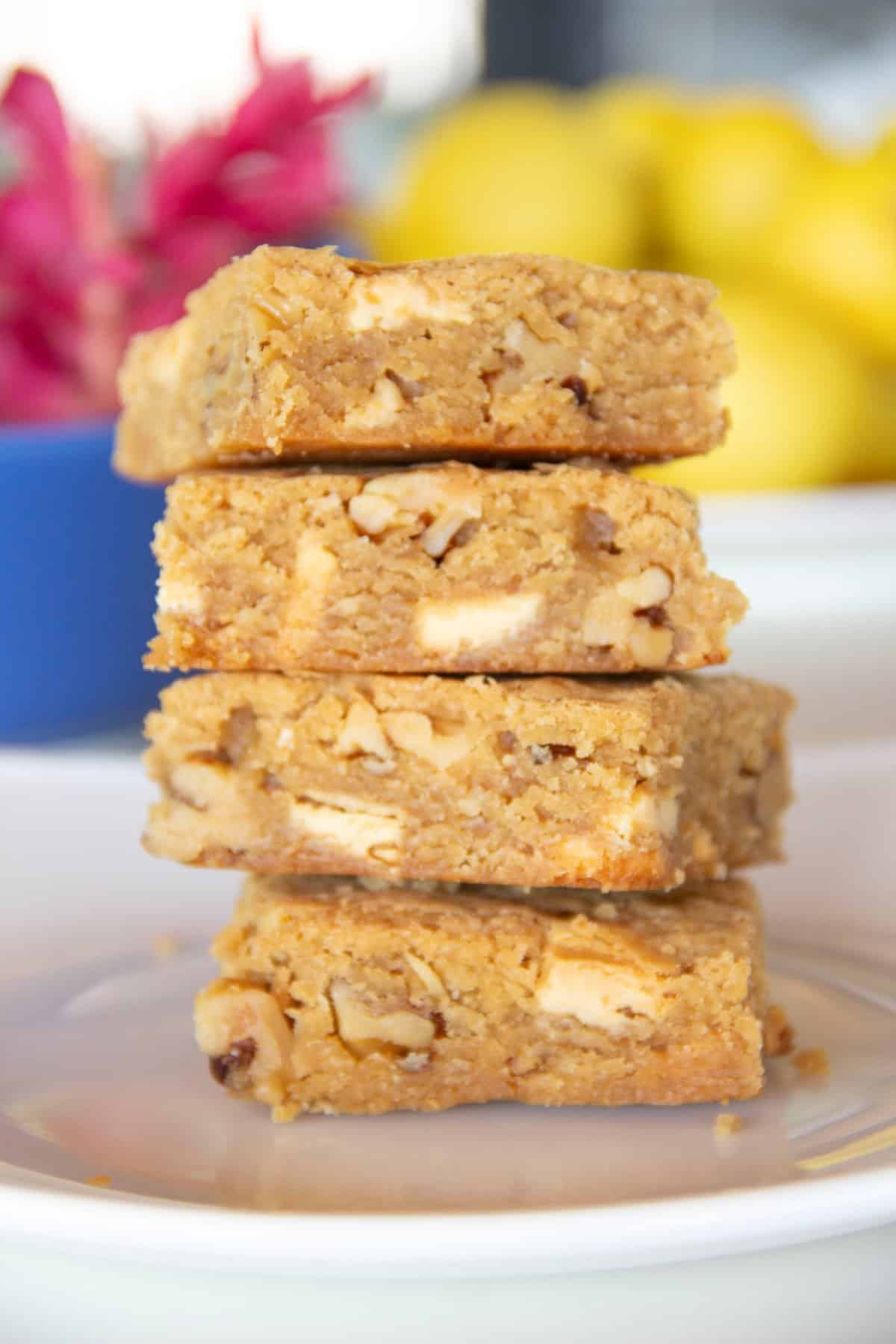 four blondies with walnuts and white chocolate chunks stacked on a plate