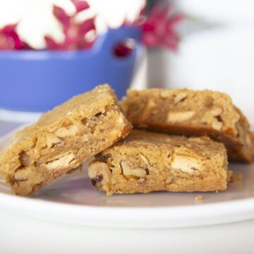 three blondies on a plate with red ginger flowers in a blue bowl in the background