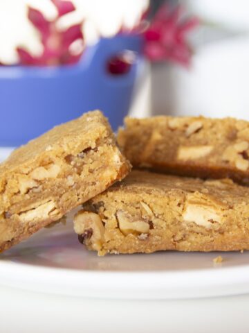 three blondies on a plate with red ginger flowers in a blue bowl in the background