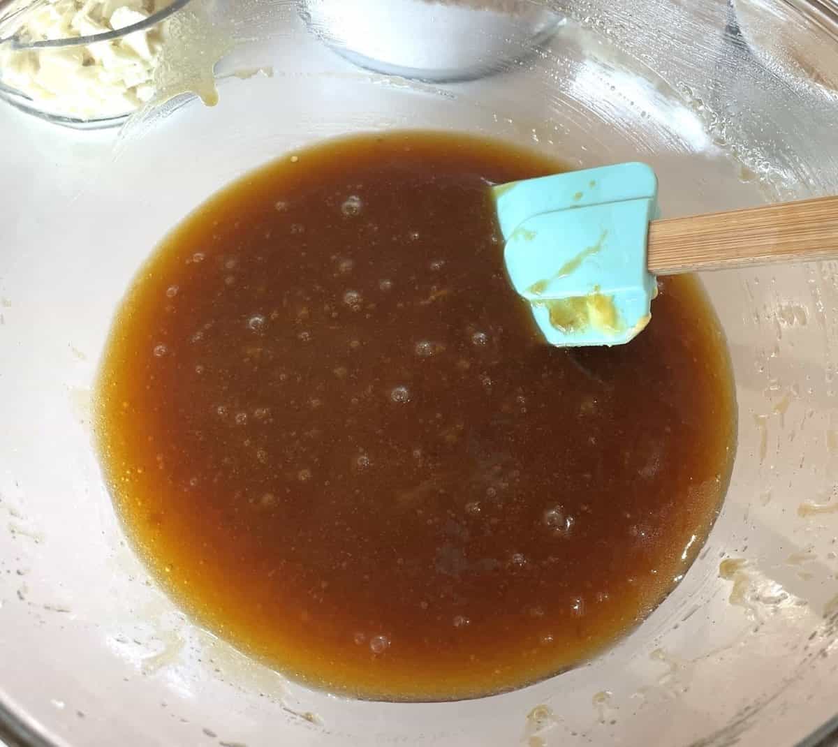 Mixing melted butter with brown and white sugars in a glass bowl
