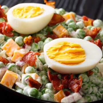 classic pea salad in a bowl garnished with bacon and hard boiled egg