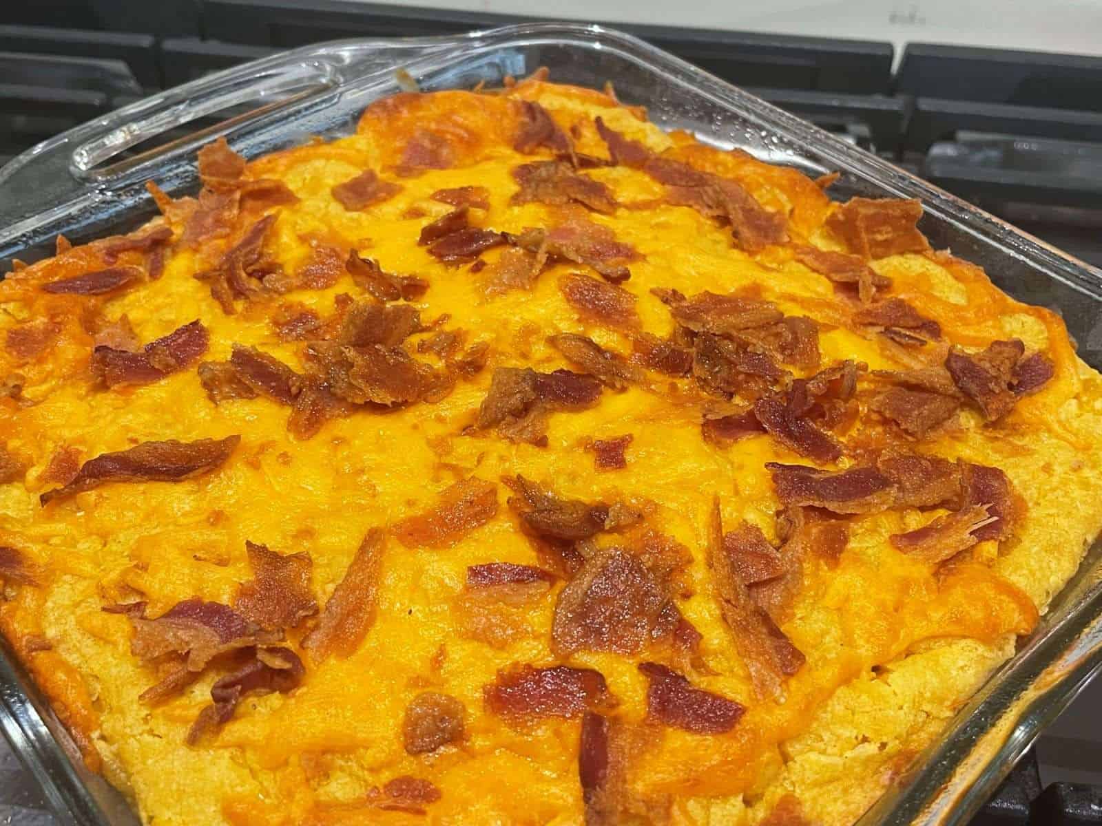 corn casserole topped with cheddar and bacon bits in a pan