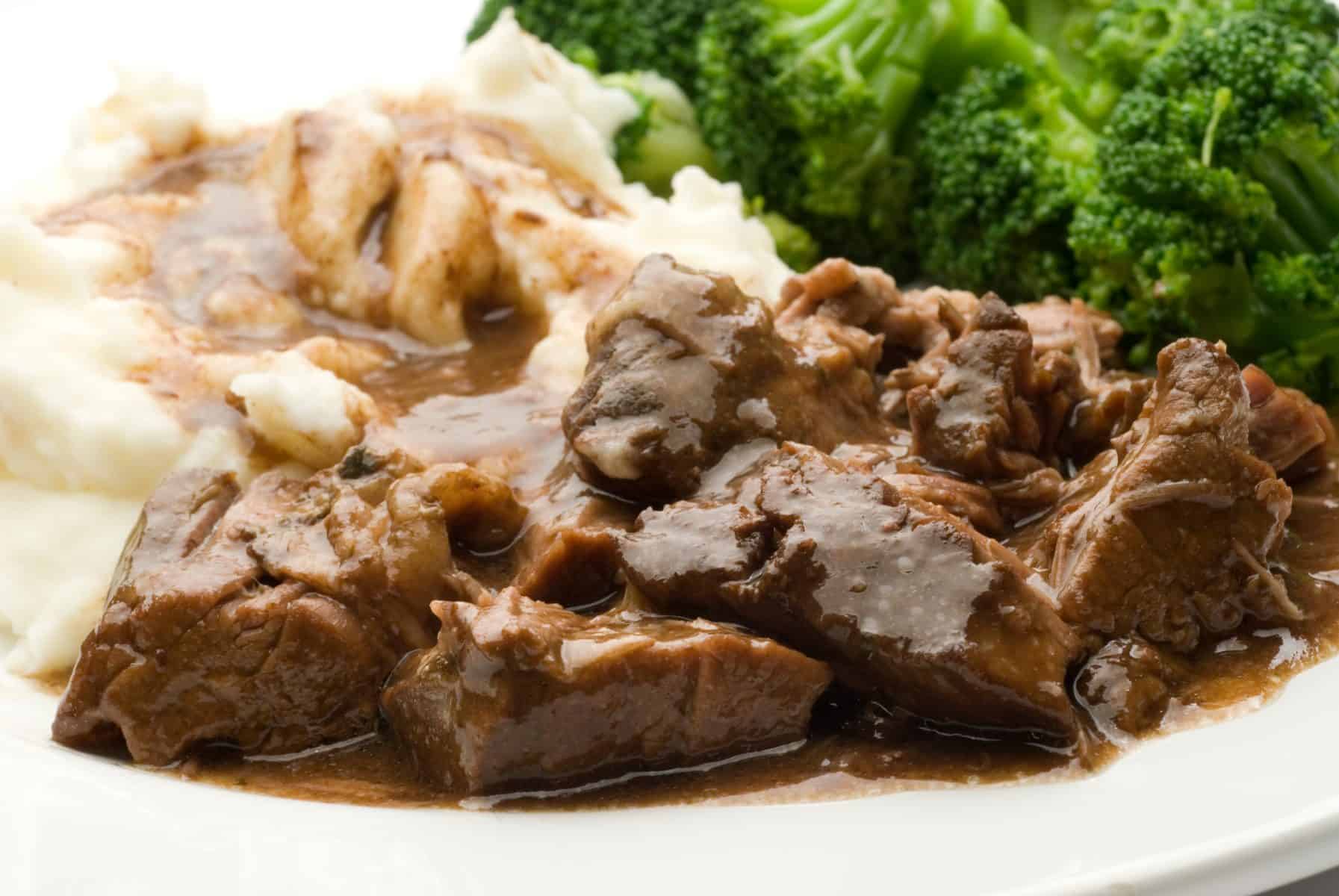 slow cooker beef roast and gravy on a plate with green beans and mashed potatoes