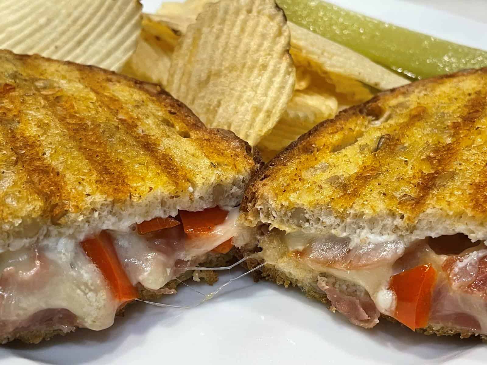 gourmet grilled cheese sandwich on a plate with chips and pickle