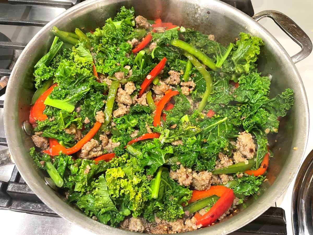 kale bell peppers and italian sausage cooking in a pan