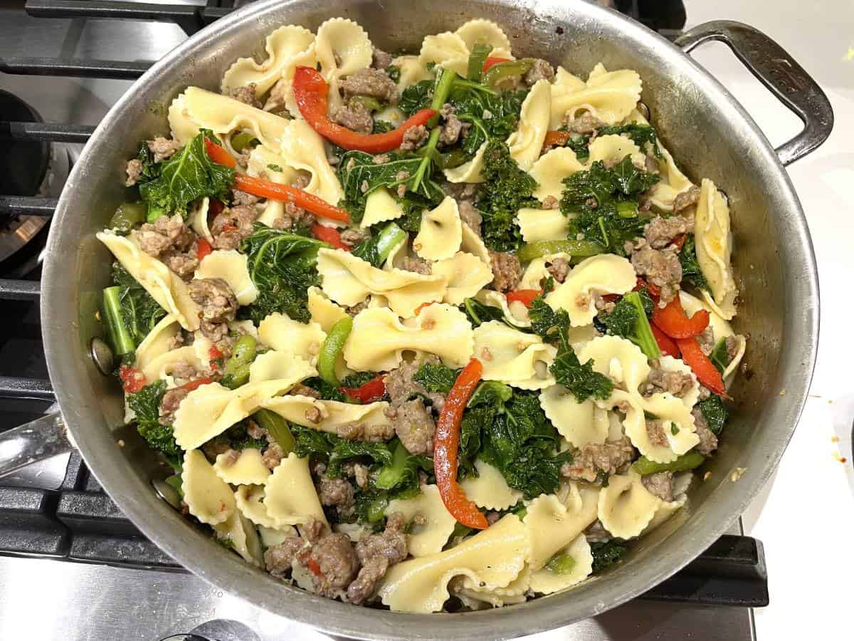 pasta kale bell pepper slices and italian sausage cooking in a pan
