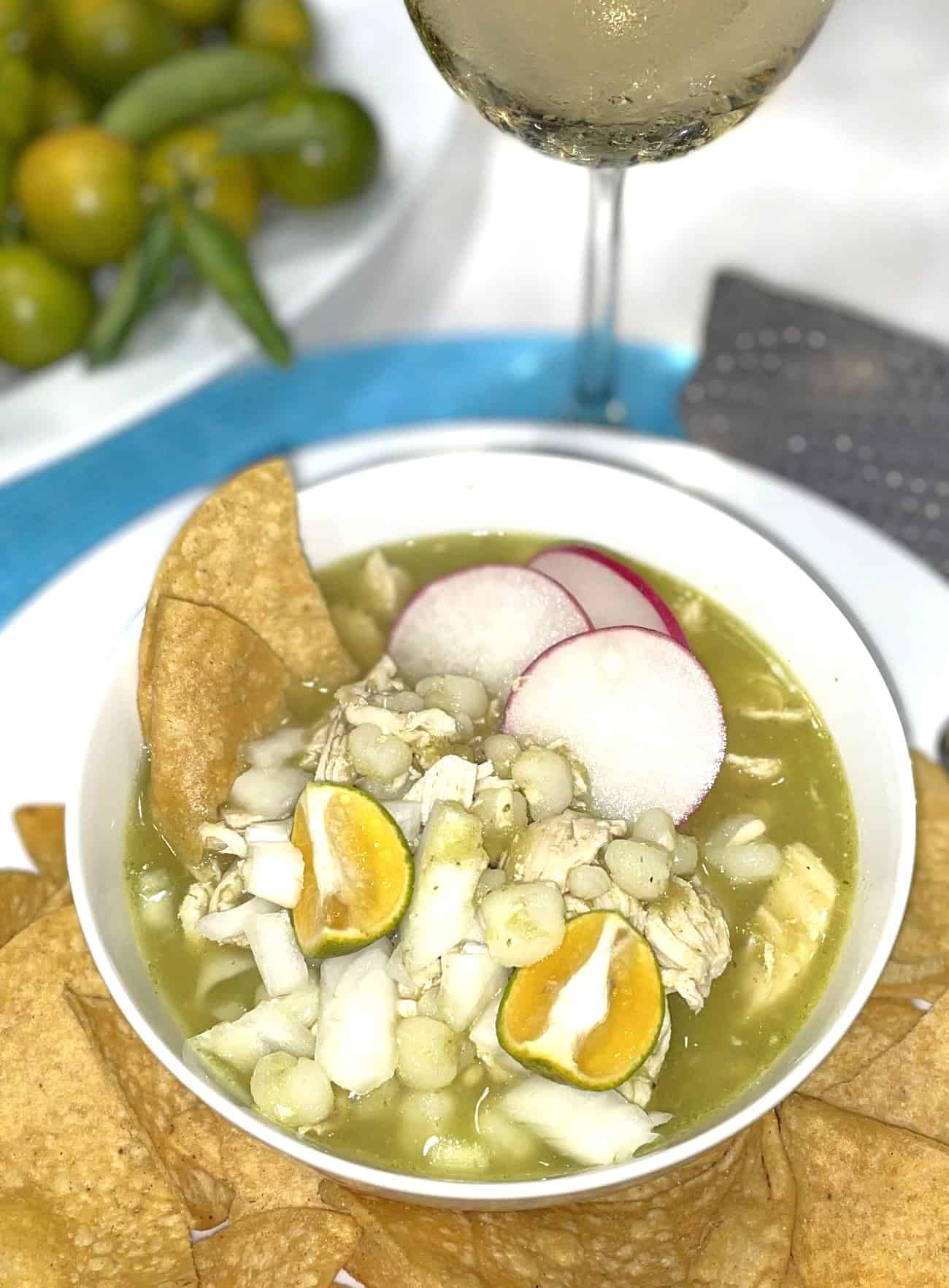 chicken pozole verde soup in a bowl garnished with tortilla chips, lime wedges and radish slices