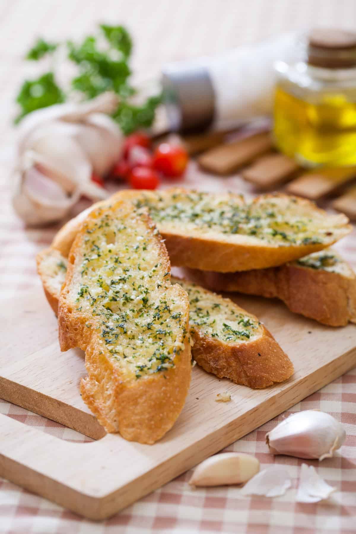 garlic bread with parsley on top on a cutting board with garlic bread ingredients in the background