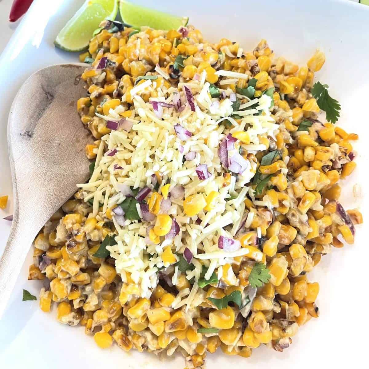 mexican street corn salad in a bowl with a wooden spoon and lime wedges