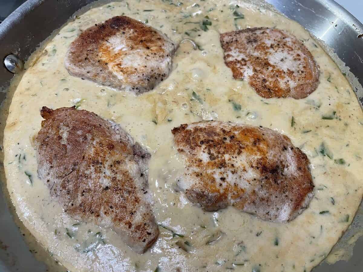 seared pork chops simmering in a pan with sour cream and parsley sauce