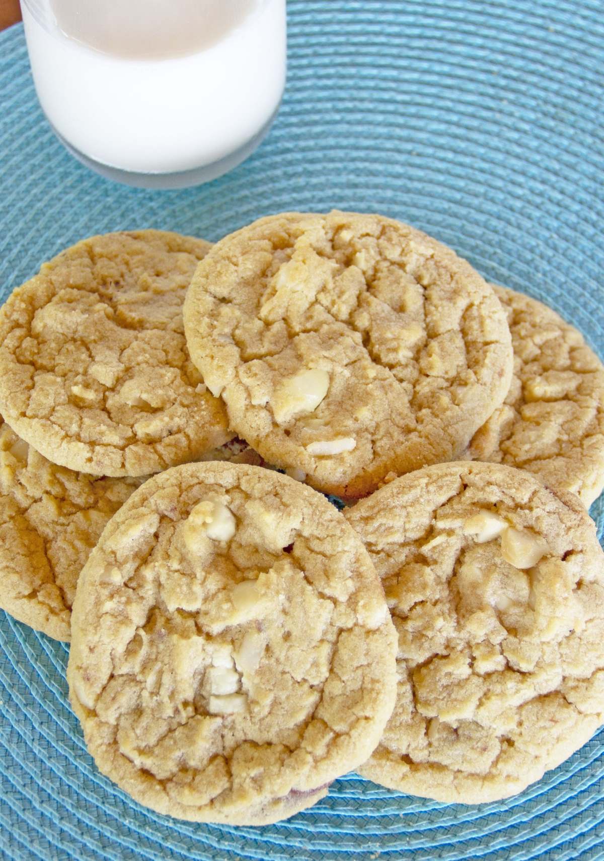 white chunk macadamia nut cookies on a light blue placemat with a glass of milk behind them
