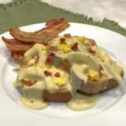 creamed eggs on toast garnished with bacon bits and slices of bacon on the side