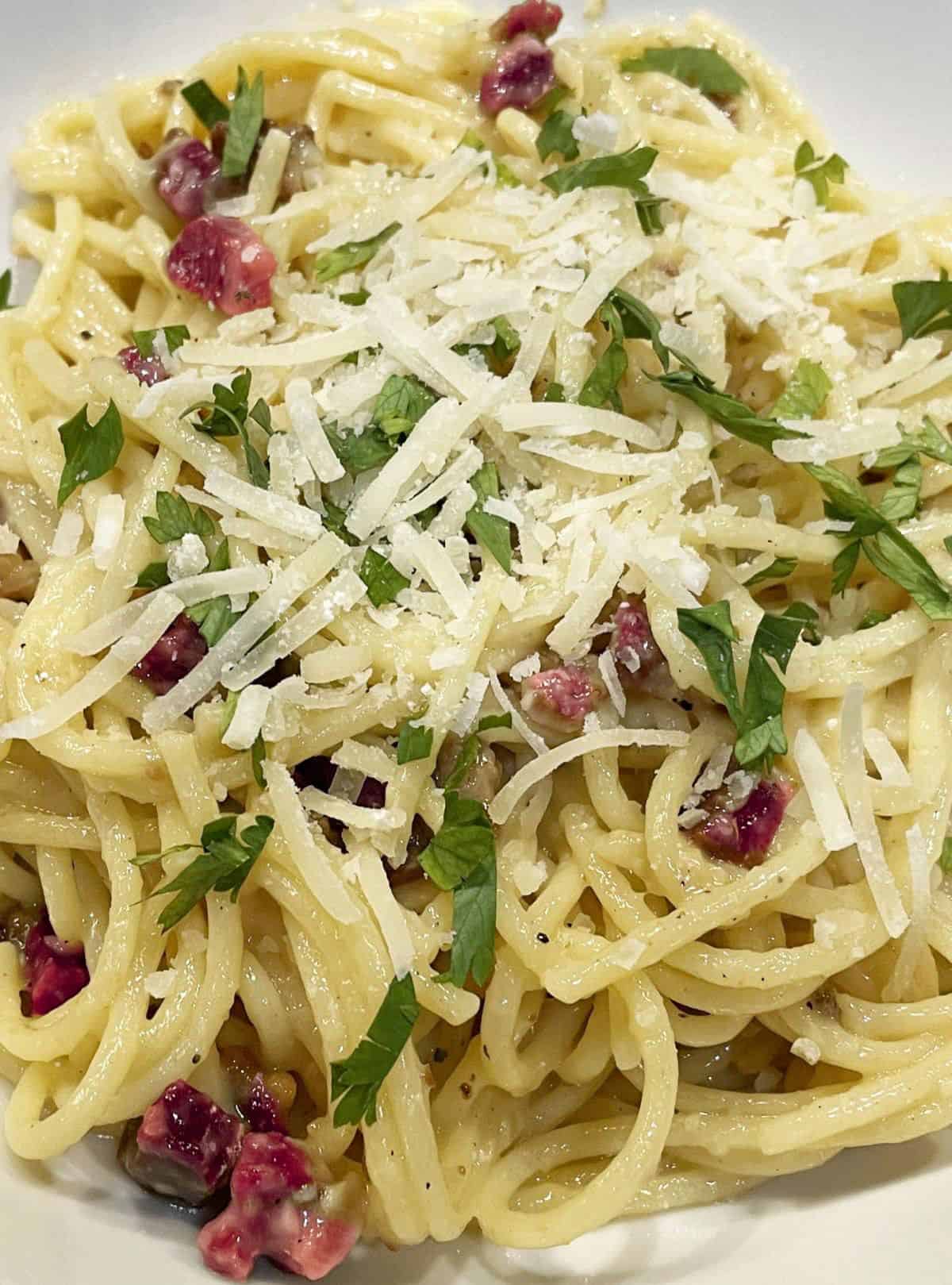 spaghetti carbonara in a wide white bowl garnished with grated parmesan and chopped parsley